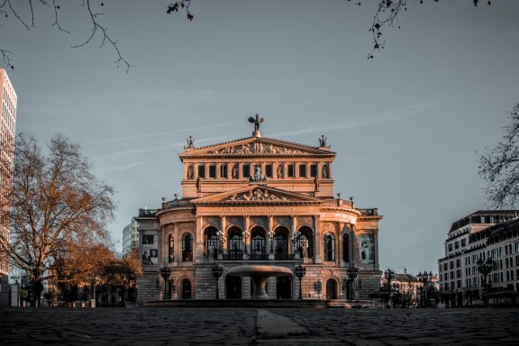 Historisches Operngebäude mit Säulenfassade, umgeben von Bäumen und städtischer Umgebung.