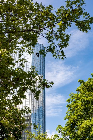 Moderner Glasturm zwischen üppigem Grün und blauem Himmel.