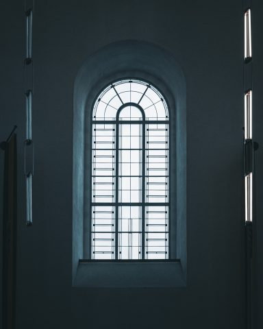 Fenster mit geschliffenem Glas und vertikalen Lamellen in einem dunklen Raum.