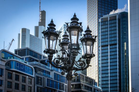 Straßenlaterne mit mehreren Lichtern vor modernen Wolkenkratzern.