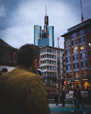 Mann betrachtet moderne Hochhäuser in einer städtischen Umgebung bei bewölktem Himmel.
